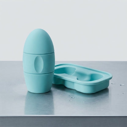 A light blue silicone baby bottle and matching silicone cup or mold set, shown on a metallic gray surface against a light gray background.