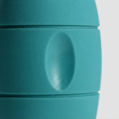 Close-up of a teal-green insulated container or bottle with a matte finish and horizontal ridges, showing a central oval protrusion on a light gray background.